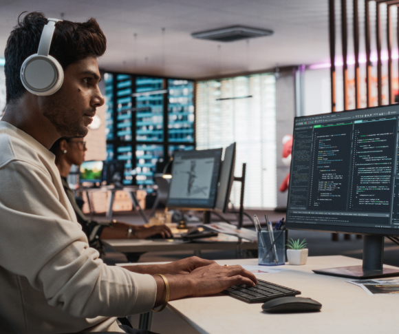 Man looking at a computer monitor wearing headphones.